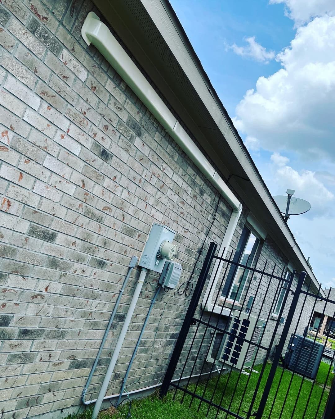 Exterior view of a brick house featuring drainage pipes and a satellite dish. Green grass visible.