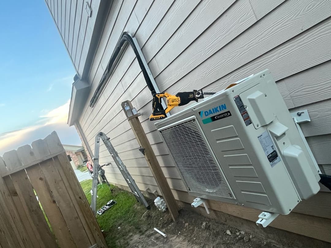 Daikin air conditioning unit installed on exterior wall with tools and ladder nearby.