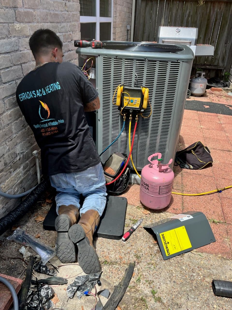 Technician repairing an air conditioning unit outdoors with tools and equipment.
