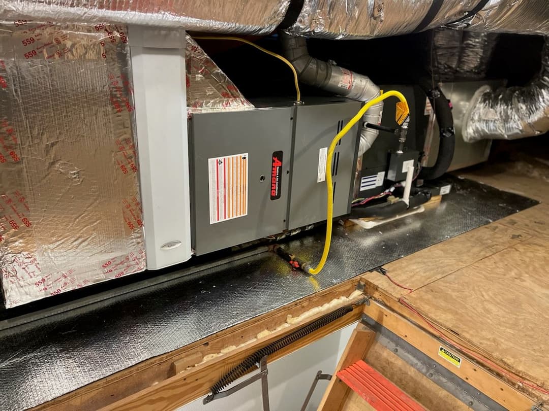 Furnace installation in attic with insulation and visible ductwork and electrical connections.