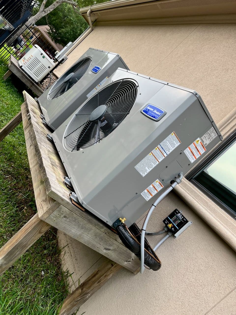 Two outdoor air conditioning units installed on a wooden platform beside a building.