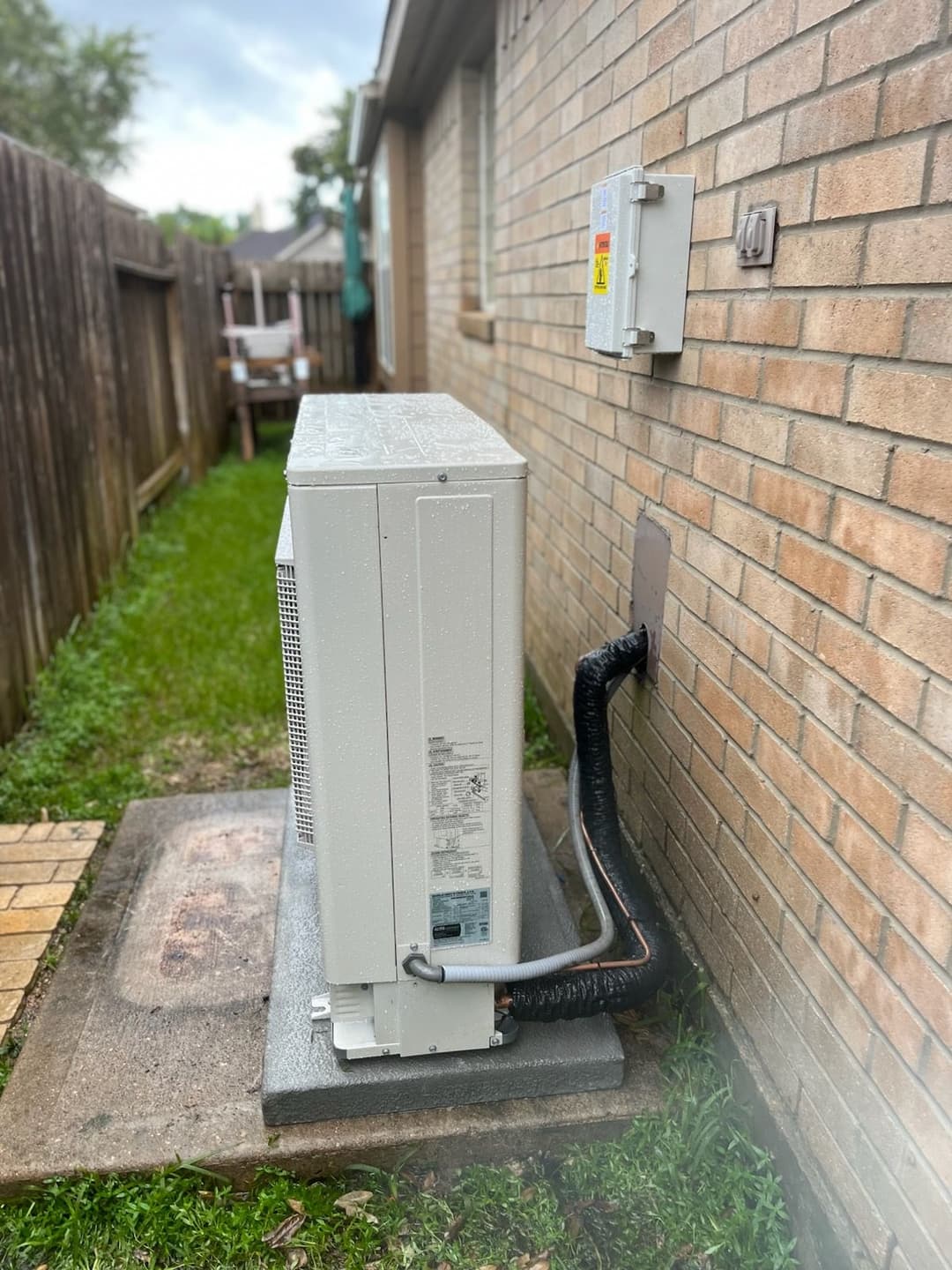 Air conditioning unit installed on the side of a house, with insulation and electrical connection.