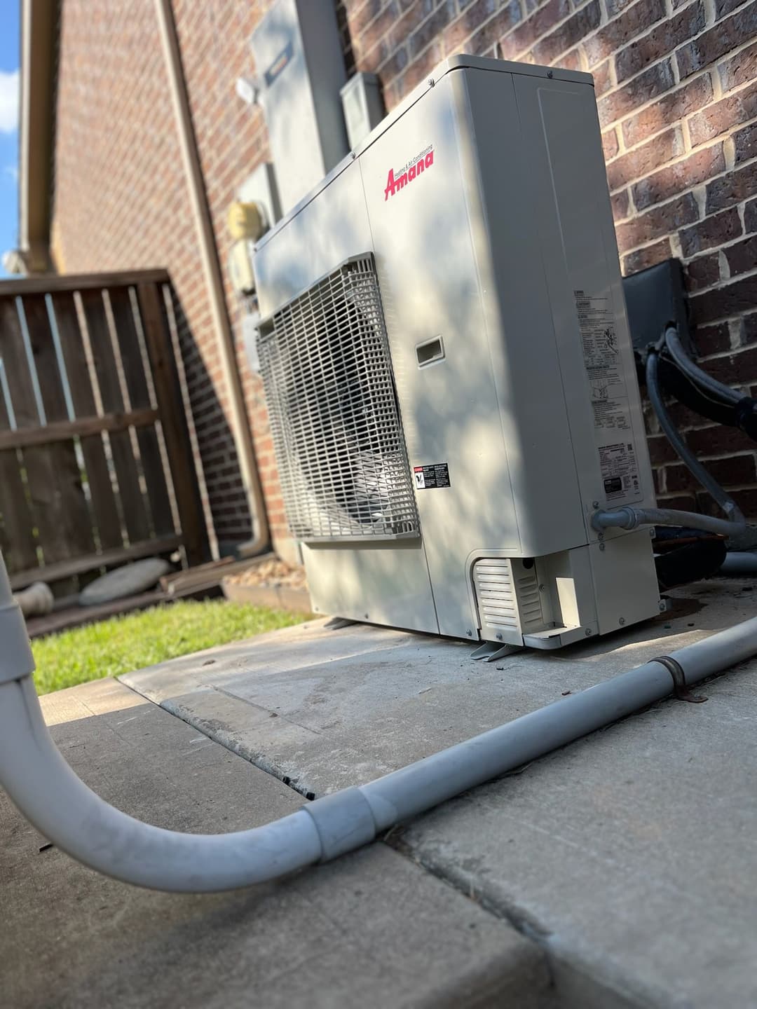 Amana outdoor air conditioning unit installed beside a brick wall and concrete patio.