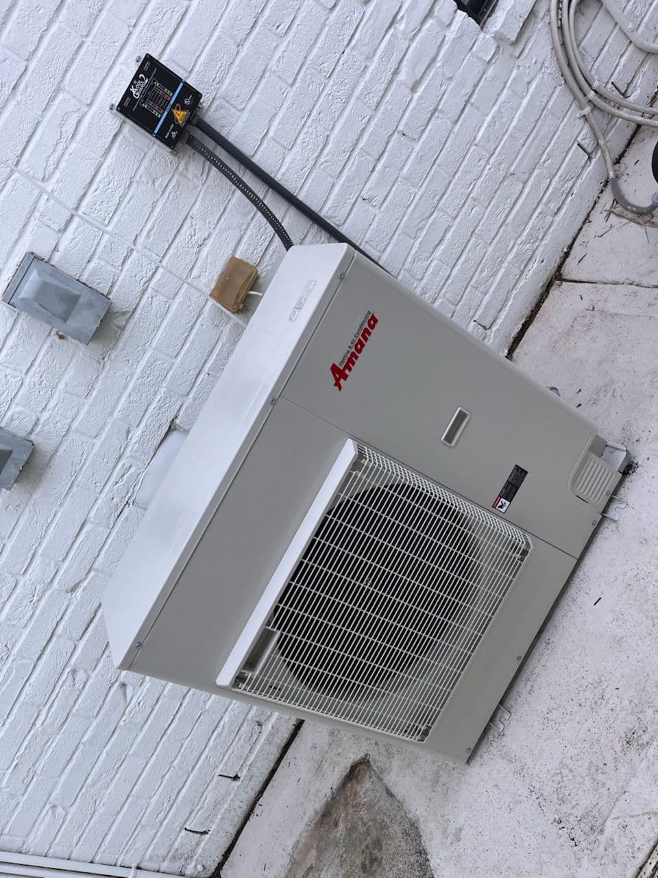 Amana air conditioning unit installed on a white brick exterior wall.