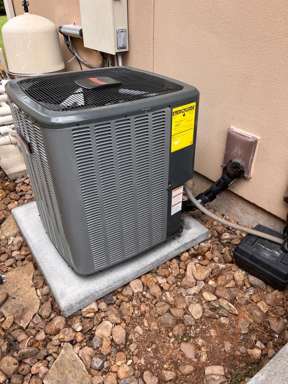Energy-efficient air conditioning unit installed outside a building, on a gravel surface.