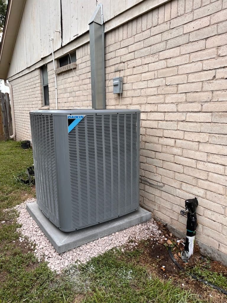 Daikin air conditioning unit installed outside a brick home, surrounded by gravel.