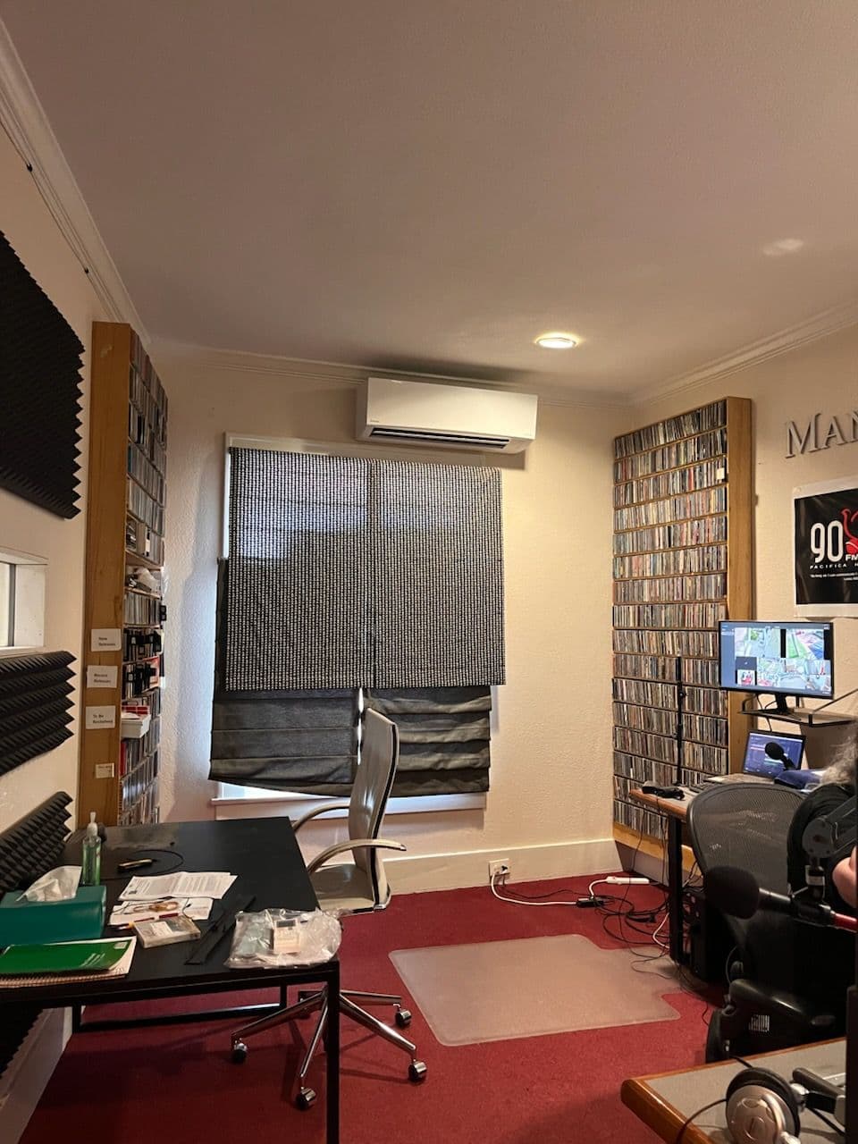 Cozy recording studio with a desk, computer, soundproof walls, and a window covered by shades.