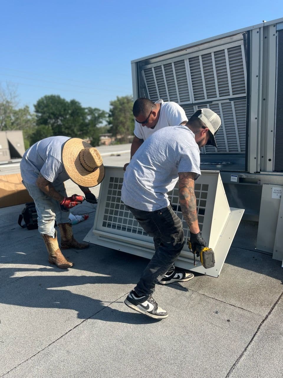 Technicians installing an air conditioning unit on a rooftop with tools and safety gear.