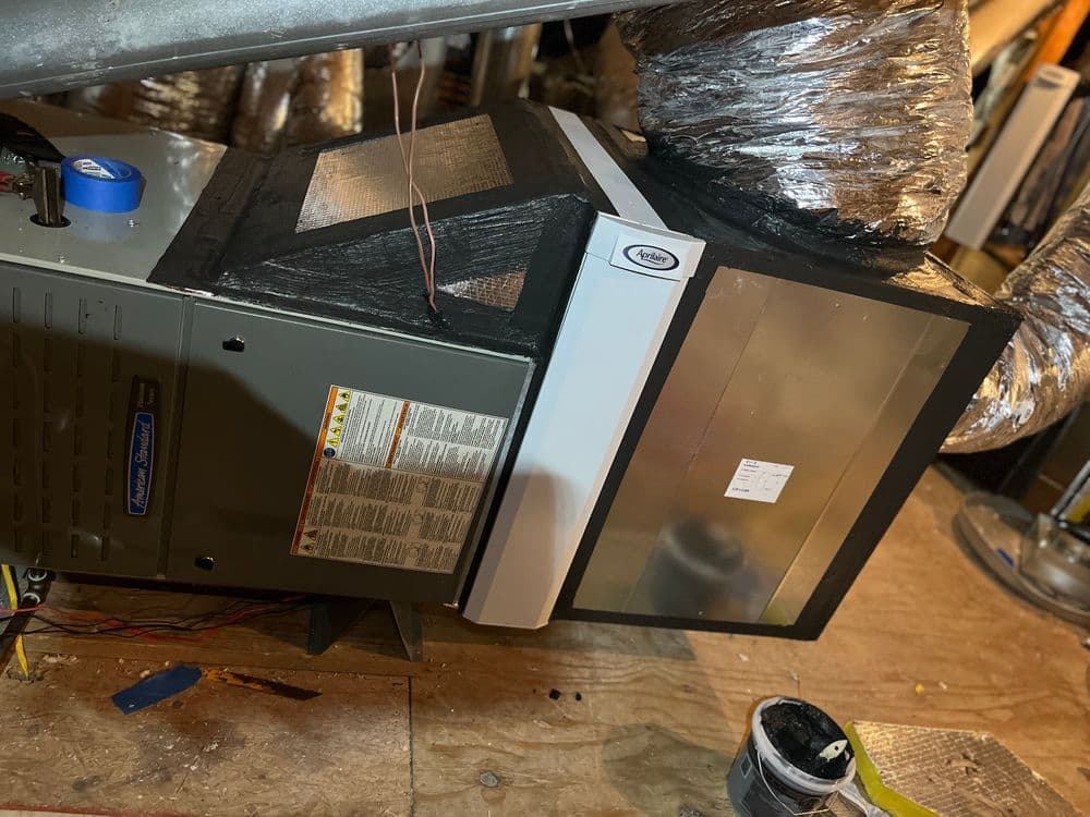 Horizontal air conditioning unit installed in a basement, with exposed ductwork and markings.