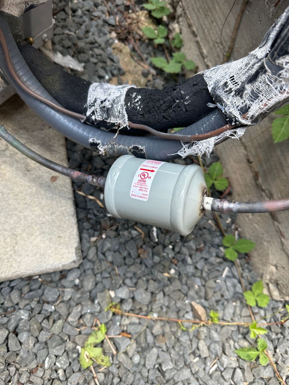 Gray capacitor on electrical lines near stone gravel, showing wear and tear on insulation.
