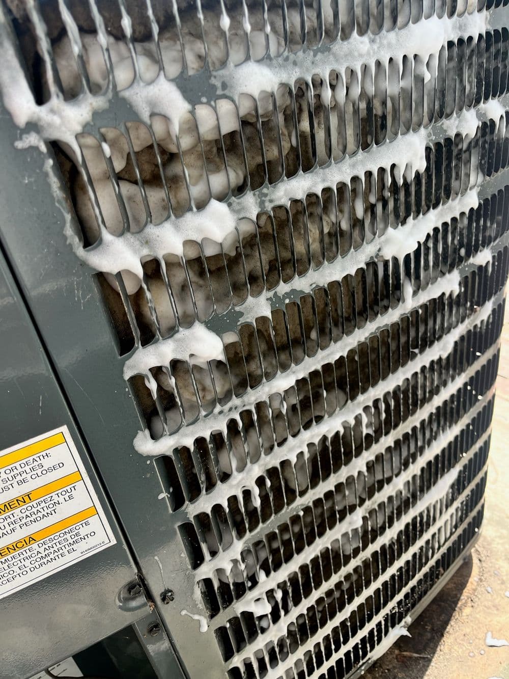 Foamy cleaning solution on air conditioning unit's exterior coils during maintenance.