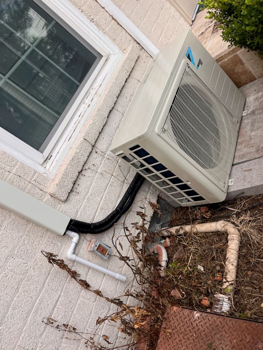 Air conditioning unit installed outside a home, showcasing pipes and landscaping.