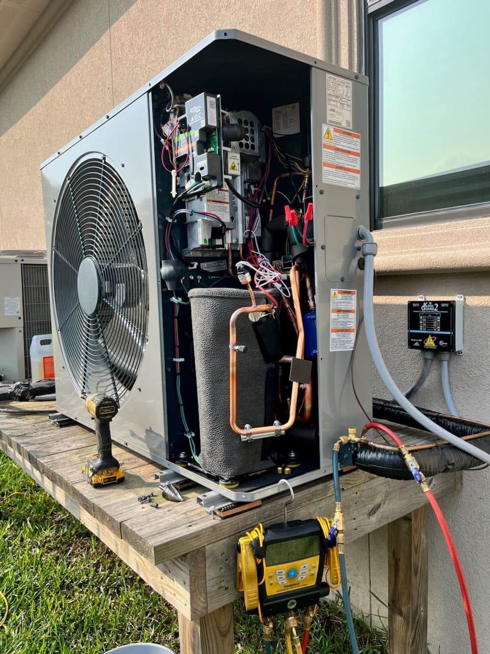 Air conditioning unit with visible internal components on a wooden platform outside a building.